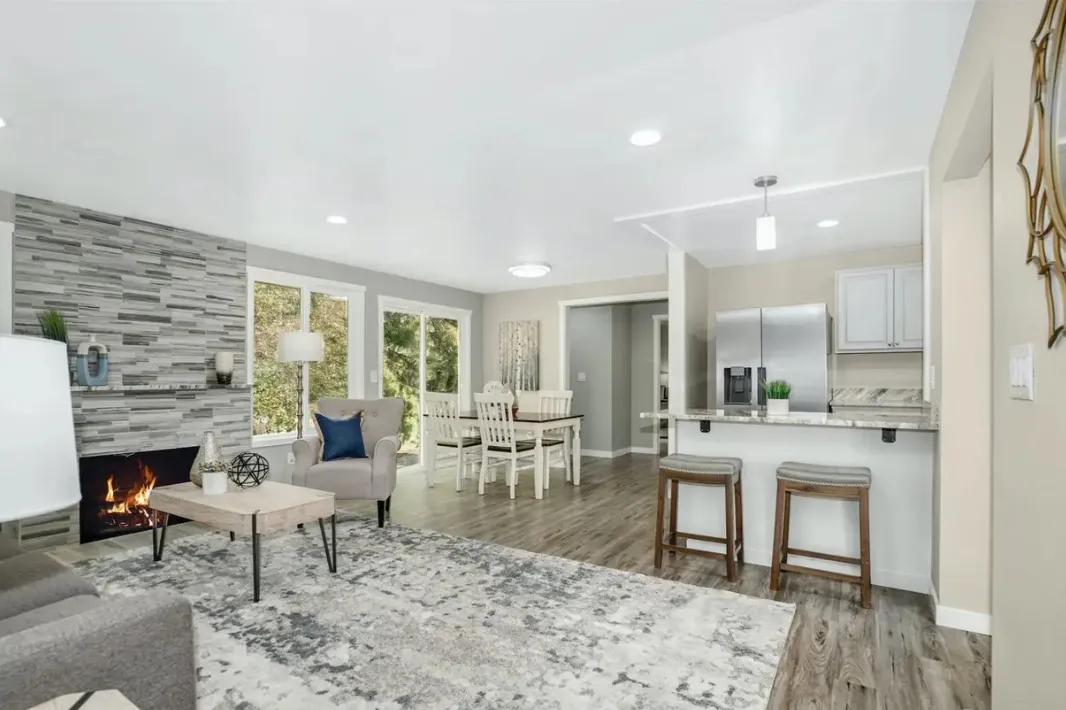Open living room with a stone fireplace, dining area and kitchen, finished with gray plank floors